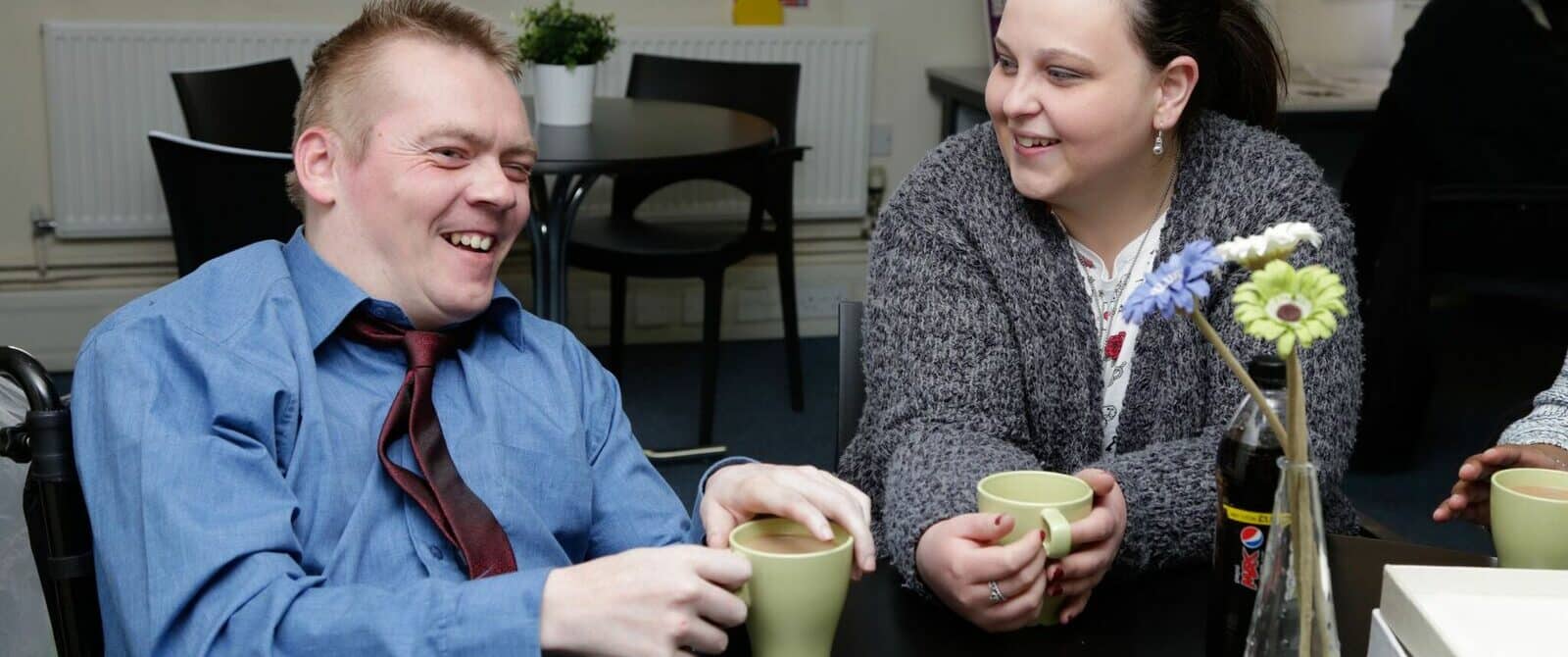 Two people - one in a wheelchair - talking over coffee.
